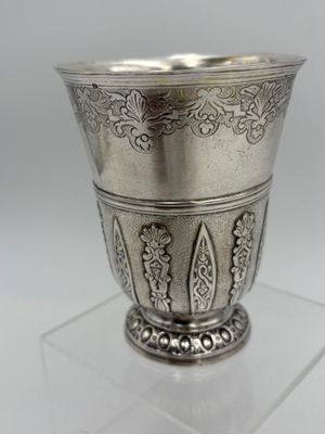 une coupe en argent ancien posée sur un socle transparent, sur une surface blanche