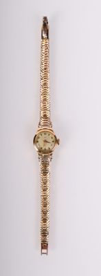 une montre-bracelet en or accrochée à un mur blanc