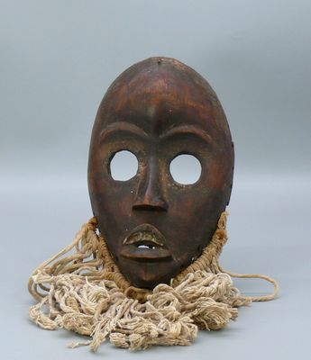 un vieux masque en bois entouré d'une corde, posé sur une surface grise