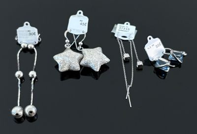 trois paires de boucles d'oreilles en argent et une paire de boucles d'oreilles en argent posées sur un fond noir