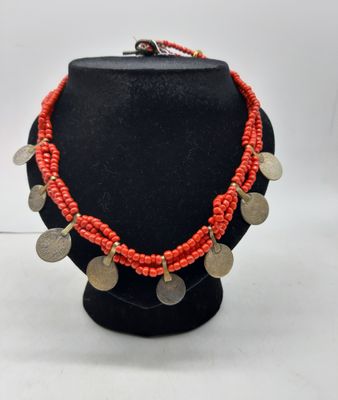 un collier composé de pièces de monnaie et de perles de corail, présenté sur un mannequin noir