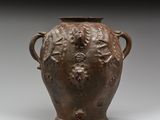 un vieux vase marron muni d’anses, sur un fond gris