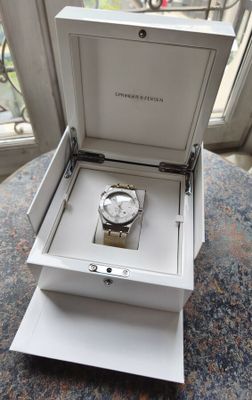 une montre dans une boîte, posée sur une table près d'une fenêtre