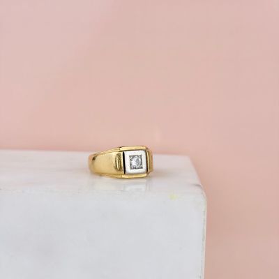 Une bague en or sertie d'un diamant taille princesse repose sur un bloc de marbre blanc