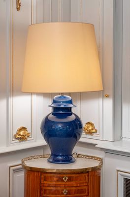 a blue vase sitting on a table with a lamp on top of it