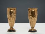 pair of gold vases on a white table with a gray background