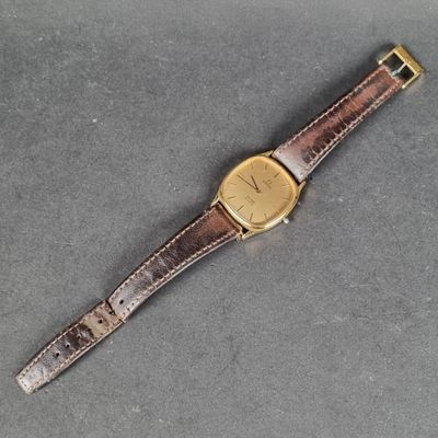 un gros plan d'une montre posée sur une surface grise, avec un bracelet marron