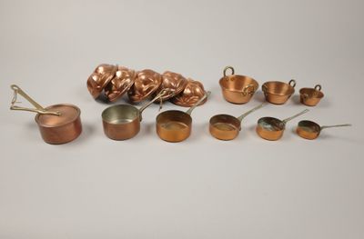 an assortment of copper pots and pans on a white surface