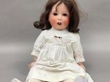 une poupée ancienne en porcelaine, assise par terre, vêtue d'une robe blanche