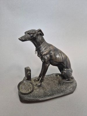 statue d'un chien assis sur un rocher, à côté d'un morceau de métal