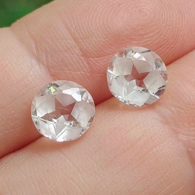 une paire de boucles d'oreilles à clous en topaze blanche et diamants au doigt d'une personne