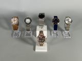 five different watches on display on a clear stand