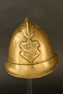 casque de pompier en laiton posé sur un socle transparent avec un fond noir