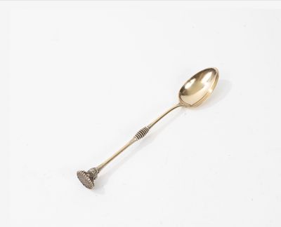 une cuillère ancienne en argent avec un manche, posée sur une surface blanche