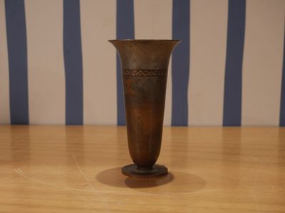 un vase marron posé sur une table en bois, avec un mur rayé en arrière-plan