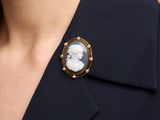 a close up of a woman wearing a black suit and a white cameo broocher