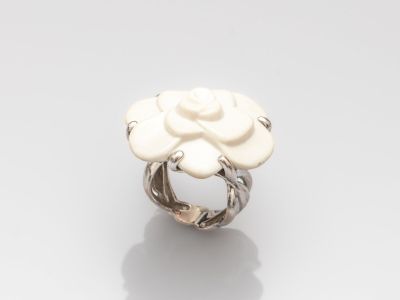 une image représentant une bague ornée d'une fleur blanche posée sur une surface blanche