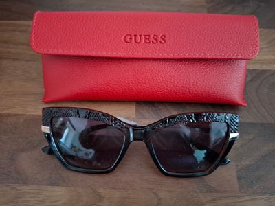Des lunettes de soleil « Guess » et leur étui posés sur une table en bois