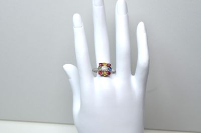 une main blanche sur laquelle se trouve une bague ornée d'un anneau multicolore