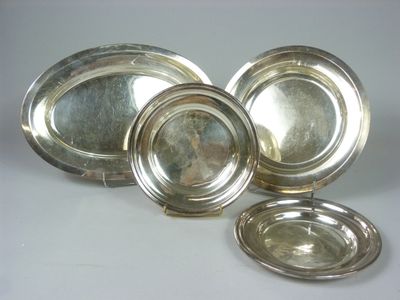 trois plats en métal argenté et une assiette en argent sur un fond blanc
