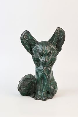 une statue verte représentant un chat assis sur une surface blanche