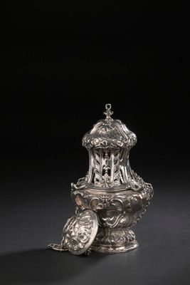 un vase en argent surmonté d'un oiseau, posé sur une surface noire