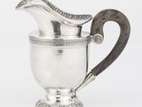 un pichet ancien en argent muni d'une poignée en bois, sur fond blanc