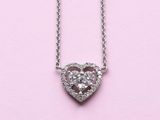 a close up of a heart shaped diamond necklace on a pink background
