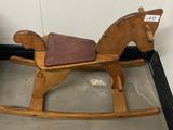 un cheval à bascule en bois avec une selle marron dans une pièce