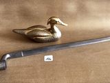 a small metal duck sitting next to a knife on a brown cloth