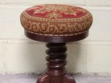 un petit tabouret en bois sur lequel est posé un coussin rouge et doré