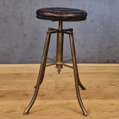 une photo d'un tabouret avec une assise en cuir posé sur un plancher en bois