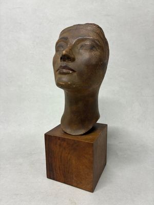 une image représentant une sculpture en bronze représentant une tête, posée sur un socle en bois