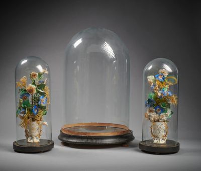 trois cloches en verre contenant des fleurs, posées sur un support en bois