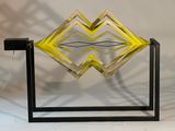 une sculpture jaune et noire posée sur un socle, devant un fond blanc