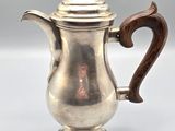 an antique silver coffee pot with a wooden handle on a white surface