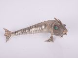 silver fish broochle with green eyes on a white surface