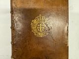 un vieux livre brun portant un emblème doré