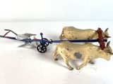 two figurines of cows pulling a cart on a white surface