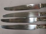 four silverplated knives are lined up on a white surface