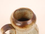a brown and white vase with a handle on a table
