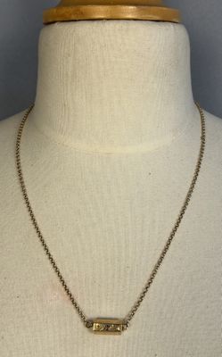 a gold necklace with a bar pendant on a mannequin neck