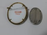 a silver and gold brooch with a pin on it