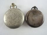 two silver pocket watches sitting side by side on a white surface