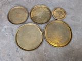 six plateaux en laiton avec leurs couvercles sont posés sur une surface en ciment