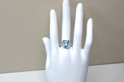 une main de mannequin blanche ornée d'une bague en topaze bleue