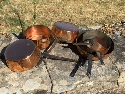 Des casseroles et des poêles sont posées sur une dalle de pierre à l'extérieur