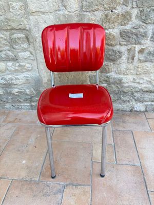 une chaise rouge posée sur un sol en briques, près d'un mur en pierre