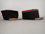 pair of black military hats with red trims on a white surface