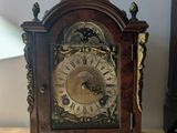 une petite horloge en bois posée sur une table à côté d'une lampe
